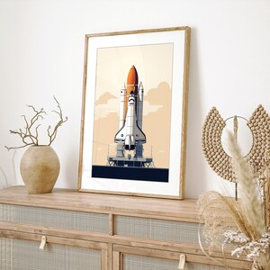Pu&ograve; includere: Stampa artistica incorniciata con un'illustrazione stilizzata di uno space shuttle su una piattaforma di lancio. L'opera d'arte ha un'estetica retr&ograve; con una tavolozza di colori arancione, bianco e blu su uno sfondo beige. La stampa &egrave; in una cornice di legno.