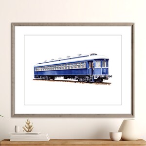 Op de afbeelding: Waterverfschilderij van een vintage blauwe passagierstreinwagon met een wit dak. De treinwagon staat op een spoor en is omlijst in een grijze houten lijst. Het kunstwerk wordt op een witte achtergrond weergegeven.