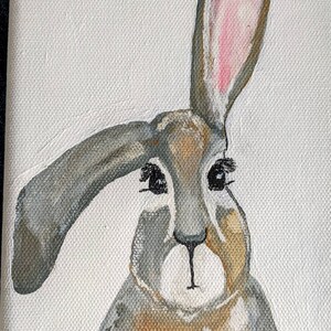 May include: A hand-painted canvas featuring a gray and brown rabbit with long ears and pink inner ears. The rabbit has large black eyes and a small black nose. The artwork is signed "Deb Burke" in the bottom right corner. The background is white.