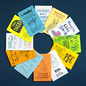 Puede incluir: Una colecci&oacute;n de diez fanzines coloridos con varios t&iacute;tulos e ilustraciones. Los fanzines est&aacute;n dispuestos en c&iacute;rculo sobre un fondo azul. Los t&iacute;tulos incluyen "The Dread", "Some of my Husband", "Like Dis", "Laundry", "Memory from a Summer", "Sometimes I Forget", "Thoughts Like Boats", "Petrified Creature Museum", "Final Resting Place", y "Voice of Dad".