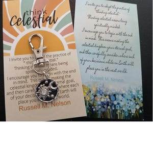 May include: A keychain with a silver charm featuring a sun, moon, and stars. The charm is attached to a silver keyring. The keychain is accompanied by a card with a quote from Russell M. Nelson that reads: "I invite you to adopt the practice of thinking celestial. Thinking celestial means being spiritually minded. I encourage you to begin with the end in mind. This means making the celestial kingdom your eternal goal, and then carefully consider where each of your decisions while on Earth will place you in the next world."