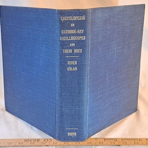 May include: A vintage blue hardcover book titled "Encyclopedia on Cathode-Ray Oscilloscopes and Their Uses" by Rider and Uslan. The book's spine displays the title and author's names in white lettering. The book is open, revealing its pages.