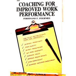 May include: A book cover titled "Coaching for Improved Work Performance" by Ferdinand F. Fournies. A clipboard with handwritten notes lists ways to improve employee results, including productivity and sales. A black pen rests on the clipboard.