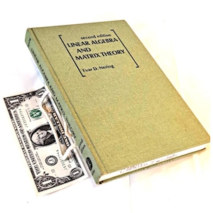 May include: A second edition textbook titled "LINEAR ALGEBRA AND MATRIX THEORY" by Evar D. Nering. The book has a green cover and is partially obscuring a one-dollar bill. The book's spine is visible, and the text is in black.