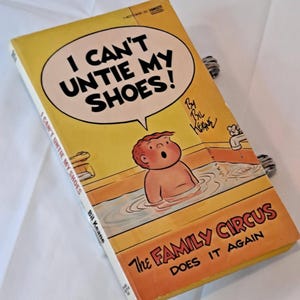 May include: A vintage paperback book titled "I Can't Untie My Shoes!" by Bil Keane. The cover features a cartoon illustration of a child in a bathtub. The book is part of "The Family Circus" series, with a yellow and orange color scheme.