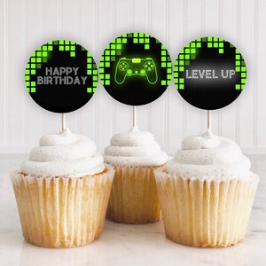 May include: Three black and green cupcake toppers with a pixelated design. The toppers say "Happy Birthday", "Level Up", and feature a green video game controller.