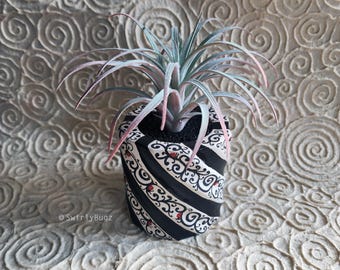 Maceta pintada a mano con rayas blancas y negras: mariquitas, espirales, planta de aire rosa/verde claro artificial.