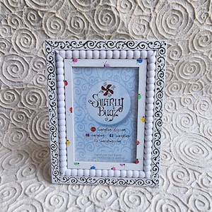 May include: White picture frame with a black and white swirl design. The frame is decorated with white beads and colorful ladybugs. The frame is 6.25 inches by 8.25 inches and fits a 4x6 inch photo.