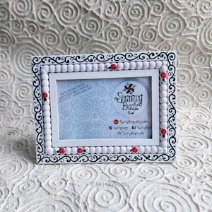 May include: White picture frame with a black and white swirl design and red ladybugs. The frame is hand painted and can be used for a 4x6 inch photo.