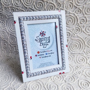 May include: White picture frame with a black and white swirl design and red ladybugs. The frame is hand painted and can be used for horizontal or vertical photos. The photo size is 4x6 inches.