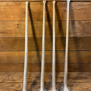 May include: Four silver metal table legs with a rounded top and a flared base. The legs are arranged in a row against a wooden background.