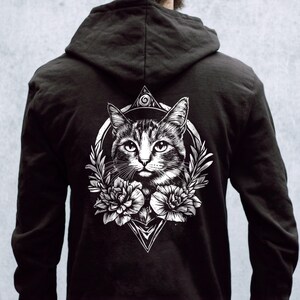 Puede incluir: Sudadera con capucha negra con un estampado gráfico blanco de la cara de un gato rodeado de flores y formas geométricas.
