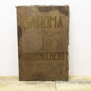 May include: A vintage brown book with gold lettering on the cover. The title is "Tacoma Commencement".