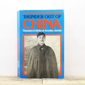 May include: A vintage book titled "Thunder Out of China" with a blue cover and orange accents. The cover features a portrait of a man in a dark coat and the names of the authors. The book is displayed on a wooden surface.