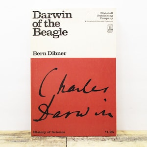 May include: A vintage book titled "Darwin of the Beagle" by Bern Dibner. The cover features a white and red design with the author's name and the words "Charles Darwin" in cursive. The book is part of the "History of Science" series.