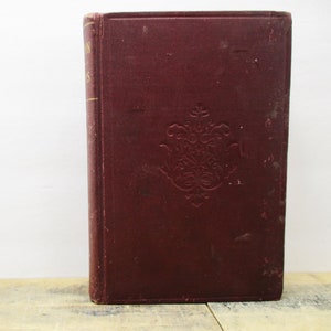 May include: A vintage, burgundy-colored hardcover book with gold lettering on the spine. The book has an ornate, embossed design on the front cover.