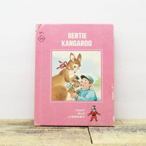 May include: A vintage children's book titled "Bertie Kangaroo" with a pink cover. The cover features an illustration of a kangaroo, a joey, and a boy in a blue outfit. The book is part of the "Tiny Elf Library" series.