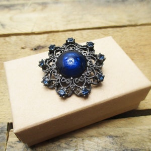 May include: A blue jeweled brooch with a large blue cabochon center stone and a filigree design.