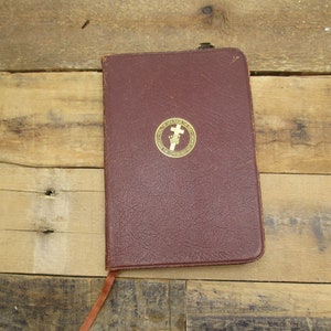 May include: A burgundy leather-bound journal with a gold embossed cross and crown design on the front cover. The journal has a brown leather bookmark attached.