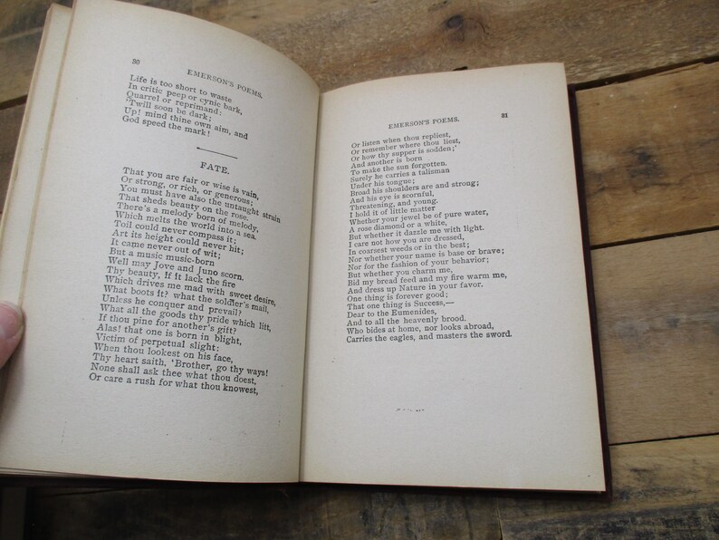 May include: An open book with yellowed pages, featuring a poem by Ralph Waldo Emerson titled "Fate". The text is printed in black ink on a white background. The book is bound in brown leather and has a worn, antique appearance.