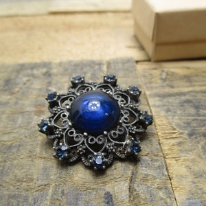 May include: A vintage brooch with a large blue cabochon stone surrounded by a filigree design and smaller blue stones.