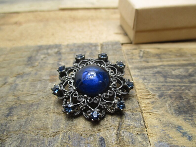 May include: A vintage brooch with a large blue cabochon stone surrounded by a filigree design and smaller blue stones.