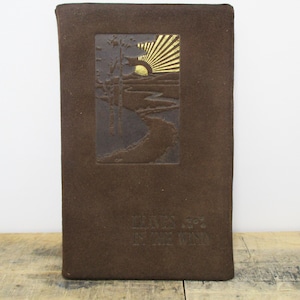 May include: A brown rectangular book cover with a rectangular inset featuring a landscape scene with a sunburst design in gold. The cover has embossed text at the bottom. The overall design is rustic and vintage.