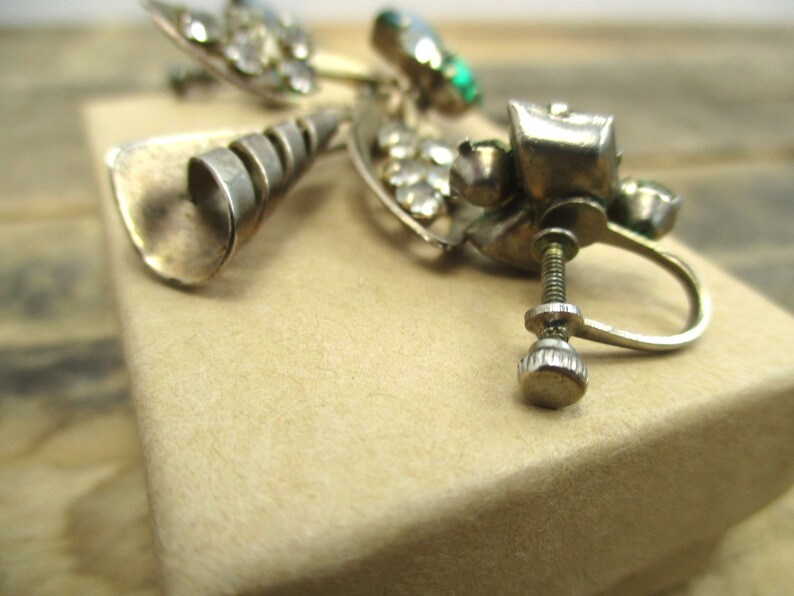 May include: Silver tone earrings with a spiral design and clear and green rhinestones. The earrings have a screw-back closure.