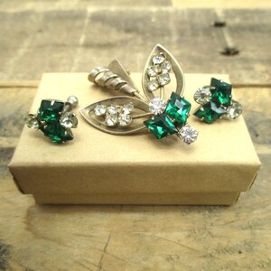 May include: A set of vintage jewelry featuring a silver brooch and earrings with green and clear rhinestones.