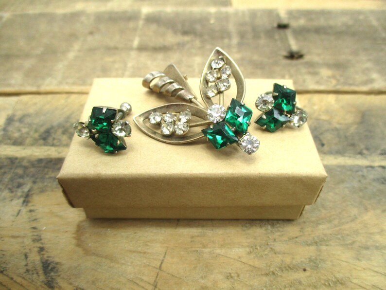 May include: A set of vintage jewelry featuring a silver brooch and earrings with green and clear rhinestones.