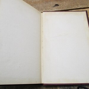 May include: An open book with blank pages and a burgundy cover. The book is lying open on a wooden surface.