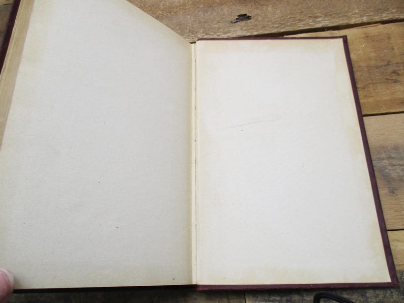 May include: An open book with blank pages and a burgundy cover. The book is lying open on a wooden surface.