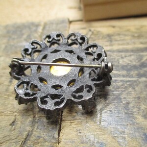 May include: A silver filigree brooch with a gold-toned center. The brooch has a pin and catch closure on the back.