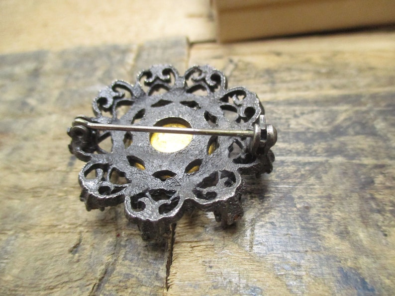May include: A silver filigree brooch with a gold-toned center. The brooch has a pin and catch closure on the back.