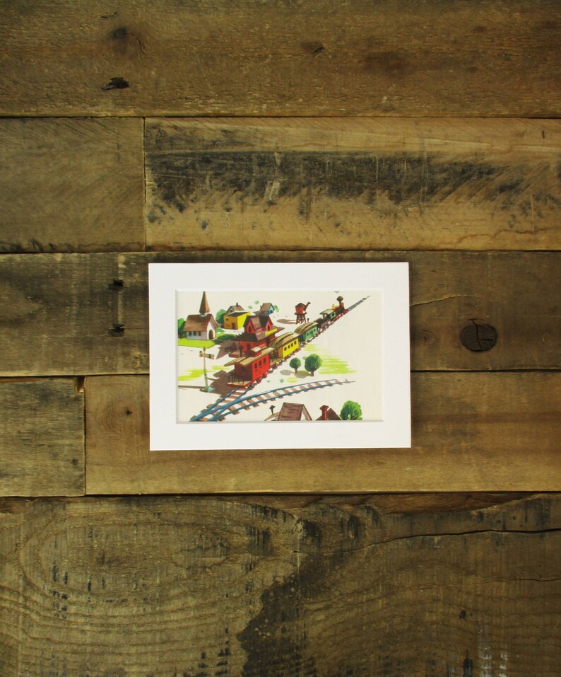 May include: A framed illustration of a train traveling through a small town. The train is made up of a red engine, yellow boxcars, and green passenger cars. The town has a church, houses, and trees.
