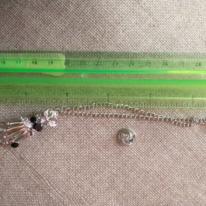 May include: A silver skeleton hand charm with black rhinestones attached to a silver chain with a safety pin clasp.