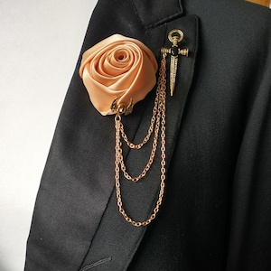 May include: A peach-coloured satin rose with gold chain accents and a gold and black dagger pin.