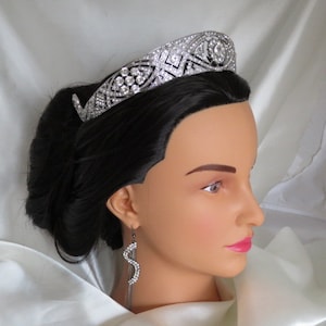 May include: A silver tiara with clear rhinestones, worn on a mannequin with black hair and dangling earrings.
