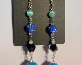 May include: Dangling earrings with a dice and billiard ball theme. Each earring features a silver hook, a teal bead, a blue die with white dots, a black faceted bead, and a blue iridescent billiard ball with the number 10 or 11.