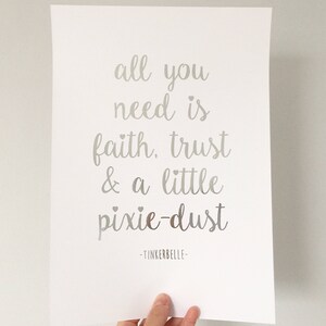 Puede incluir: Una impresión plateada con la cita "all you need is faith, trust & a little pixie-dust -Tinkerbelle" sobre un fondo blanco.
