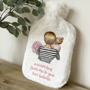 May include: White faux fur hot water bottle with a printed design of a woman and a girl holding flowers. The text "a warm hug from me to you Love Isabella" is printed on the bottle.