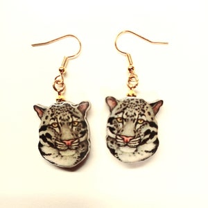 May include: A pair of gold dangle earrings with a white and gray clouded leopard head image on each earring.