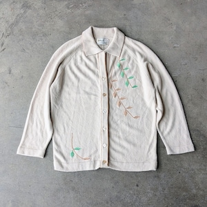 May include: Cream-colored cardigan with long sleeves and a collared neckline. The sweater features embroidered leaf designs in shades of green and brown. The cardigan has a button-up front and a label on the collar.
