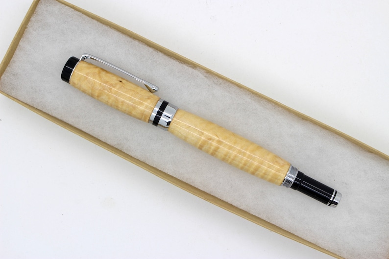 May include: A wooden pen with black and silver trim. The pen is in a brown box with white tissue paper.