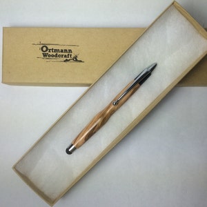 Puede incluir: Un bolígrafo de madera con una punta de lápiz táctil plateada y un recambio de tinta negro, en una caja de cartón marrón con papel de seda blanco.