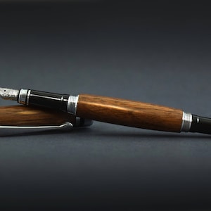May include: A wooden fountain pen with black and silver trim. The pen is lying on a dark grey surface.