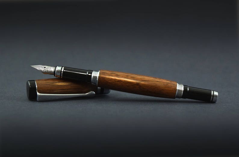 May include: A wooden fountain pen with black and silver trim. The pen is lying on a dark grey surface.