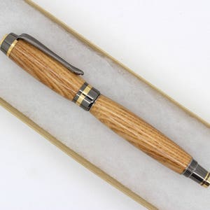 May include: A wooden pen with a black metal clip and gold accents. The pen is lying on a brown and white surface.