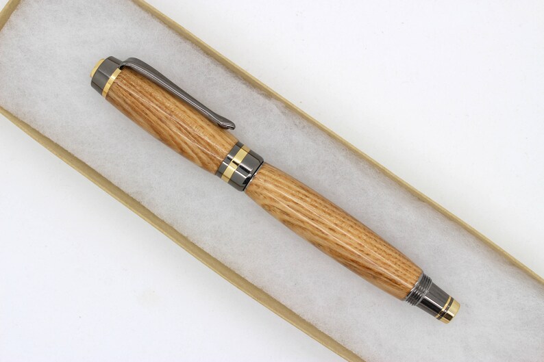 May include: A wooden pen with a black metal clip and gold accents. The pen is lying on a brown and white surface.