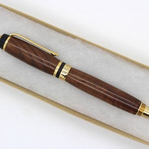May include: A wooden pen with gold accents and a black cap. The pen is in a brown box with white tissue paper.